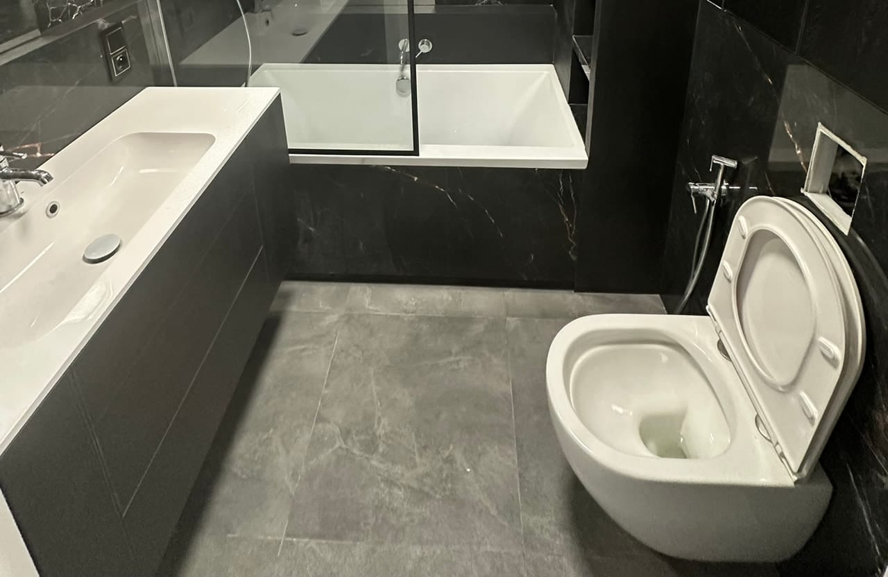 Łazienka w ciemnym marmurze z wanną, miską WC podwieszaną i umywalką blatową