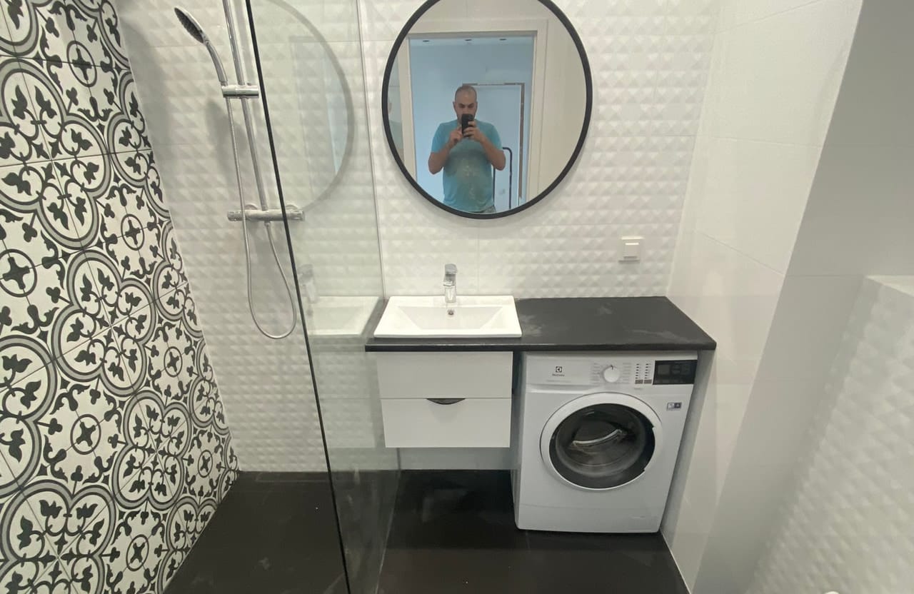 Łazienka z płytkami patchwork na ścianach i jednolitą ciemną posadzką, umywalka z pralką w zabudowie