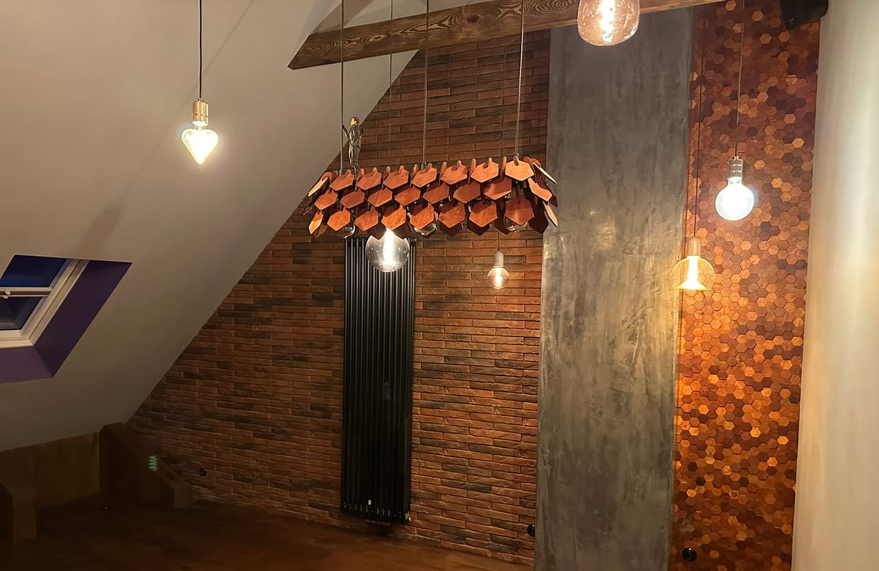Poddasze ze ścianą z cegły, pasem tynku dekoracyjnego i miedzianą mozaiką, z lampą z dachówek ceramicznych