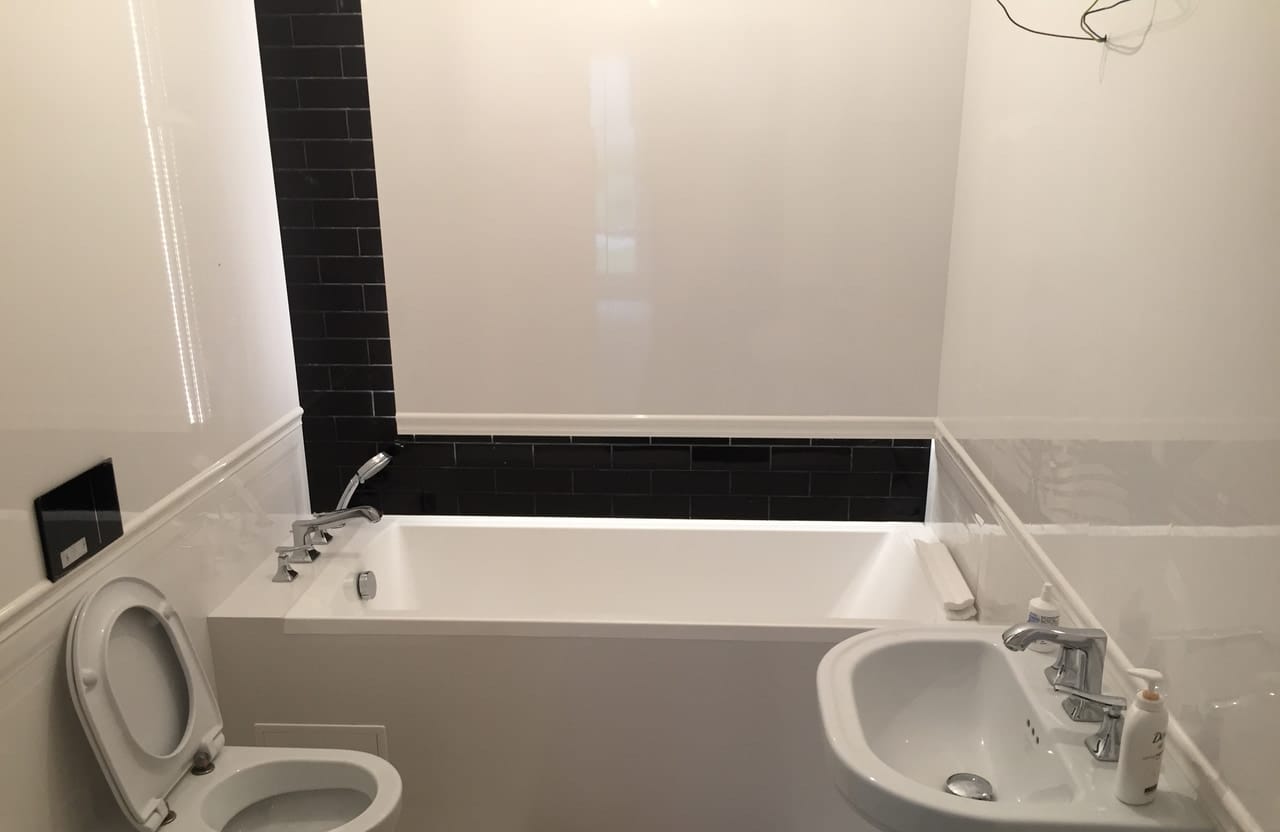 Łazienka z wanną, miską WC podwieszaną i umywalką, z ciemną mozaiką nad wanną