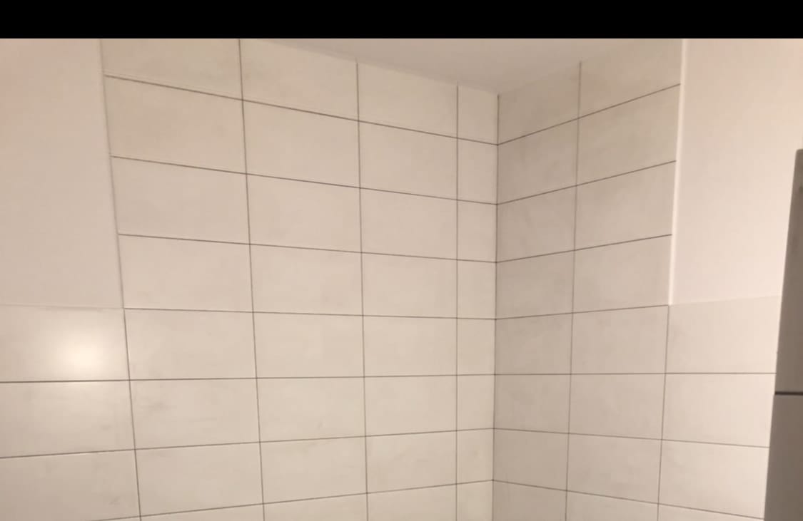 Wanna w zabudowie z białych płytek, z pasem mozaiki wzdłuż obudowy