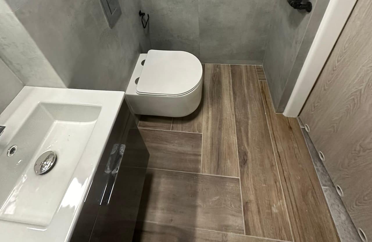 Toaleta z umywalką, miską WC podwieszaną i czarnym grzejnikiem, płytki betonopodobne i drewnopodobne