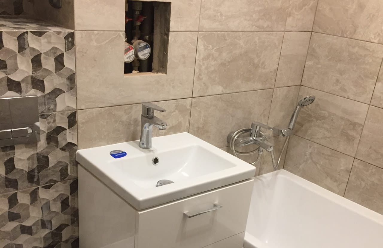 Łazienka z wanną, umywalką i pasem mozaiki o fakturze 3D na ścianie