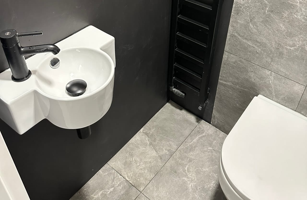 Umywalka i miska WC podwieszana przy czarnym grzejniku drabinkowym